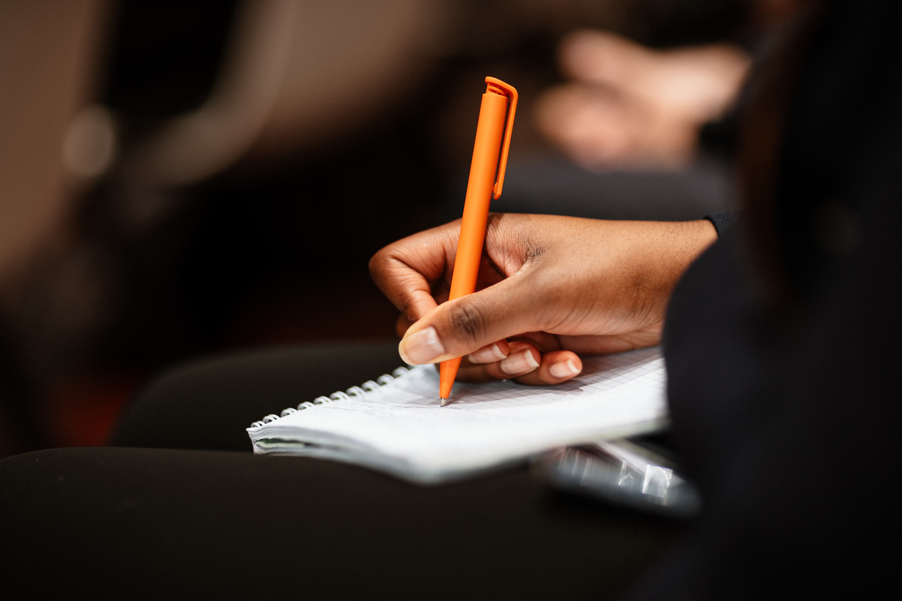 Hand writing with an orange pen representing MBA essay development